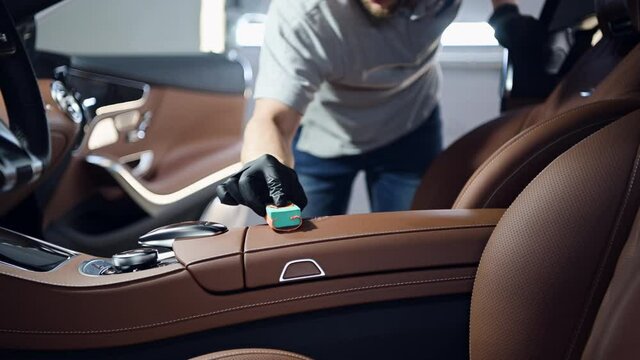 Man does car interior detaling, covering center console of a luxury car with special protective coating.