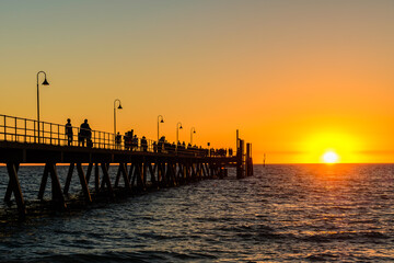Fototapeta premium Crowds of people walking along Glenelg Beach jetty at sunset time during a summer evening