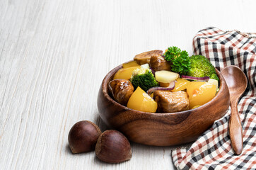 Chestnut and broccoli stir fry in wooden bowl on white table