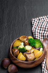 Chestnut and broccoli stir fry in wooden bowl on black stone background