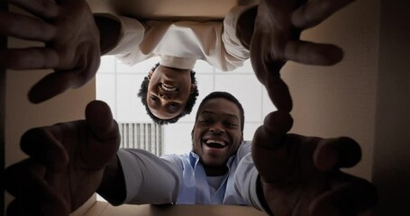 Happy ethnic mixed race couple opening big cardboard delivery box and looking inside, young afro american family wife and husband smiling cheerful rejoices with presents gifts put their hands inside