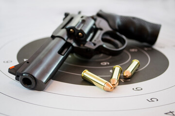 Gun revolver and golden bullets on paper target for shooting practice