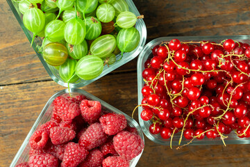 Assorted berries of raspberries, gooseberries and red currants in glass bowls on a wooden table. Top viewn