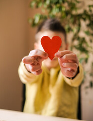 Obraz premium Boys hands in yellow t-shirt shows a handmade red paper heart 