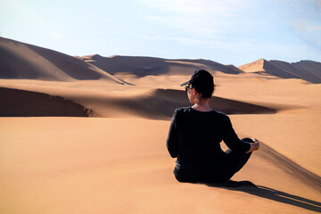A woman is sitting on the golden sand dune of the Namib desert. Africa
