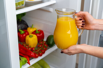 Female hand taking orange juice jar from a fridge