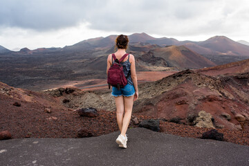 Fototapeta premium Young woman with a backpack contemplating the volcanic area Timanfaya Natural Park, in Lanzarote, travel photography
