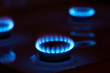 Small blue hot flame of gas burning on burner of kitchen stove at high oxygen level on dark...