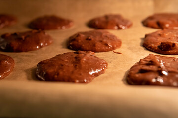 Unbaked chocolate cookie dough on a baking tray inside the oven. Pre-baked healthy gluten free brownie cookies with chocolate chips. Selective focus.