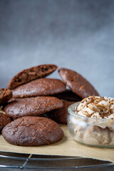 Pile of fluffy chocolate brownie cookies with a broken cookie on top served with peanut butter ice cream in a glass jar. Healthy homemade gluten free chocolate chip cookies on a cooling rack.