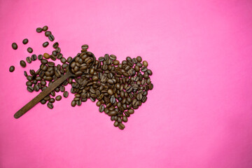 Obraz na płótnie Canvas Coffee beans in wooden spoon, heart shape. Pink background.
