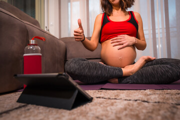 Young pregnant caucasian brunette giving thumbs up to online yoga teacher. Online exercises in prepartum classes, wellness during pregnancy