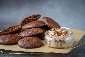 Pile of fluffy chocolate brownie cookies with a broken cookie on top served with peanut butter ice cream in a glass jar. Healthy homemade gluten free chocolate chip cookies on a cooling rack.