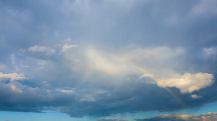 Colorful rainbow in stormy gray cloudy sky over the city