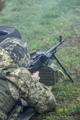 Machine gunner operator in camouflage uniform and body armor shoots from a Kalashnikov machine gun at a firing position. Shooting and training for battle concept