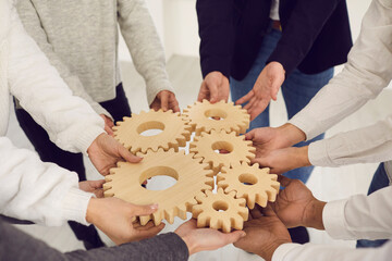 Cropped shot of group of multiethnic people joining gear wheels together as metaphor for team collaboration, unity, teamwork, finding creative solutions and creating well-functioning business system
