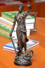 Statue of blindfolded Themis with a sword and scales in her hands, standing on a desk with books on jurisprudence in the office. Justice, human rights, advocacy, lawyering and education concept