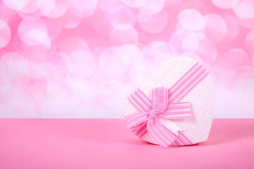 Gift in the form of a heart on a pink background with bokeh