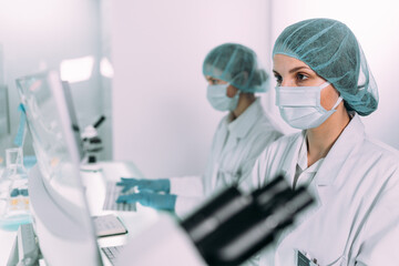 Young, female doctors working in futuristic laboratory. Using computers and microscopes