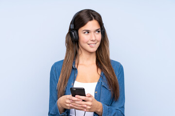 Teenager Brazilian girl listening music over isolated blue background