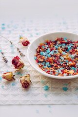 Homemade dry rose petals flower bath salt blend for aromatherapy and relaxation in bathtub, bath mix. Plate with blue color bath salt mixed with herbs and flower petals on white background. 