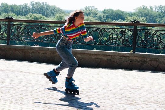 Cheerful beautiful teenage girl rollerblading in the park on a warm summer morning