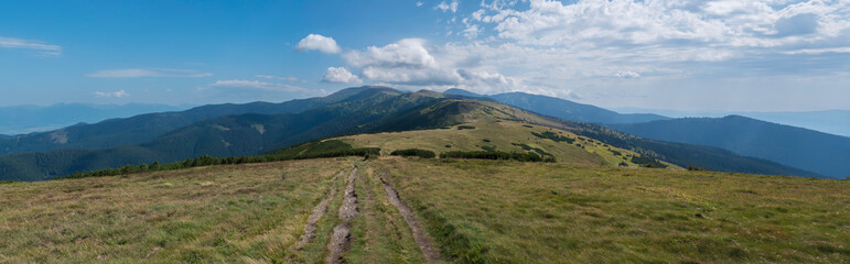 Wide panorama of grassy green hills and slopes at ridge of Low Tatras mountains with hiking trail footpath, mountain meadow, and pine scrub, Slovakia, summer sunny day, blue sky background