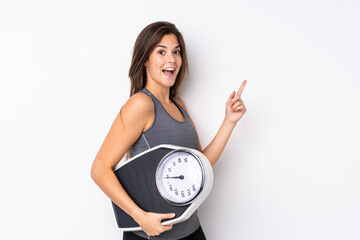 Teenager Brazilian girl holding a scale over isolated white background with weighing machine