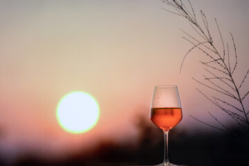 Glass of red Wine on rock with beautiful clouds of sunset or sunrise in background with blurred grass