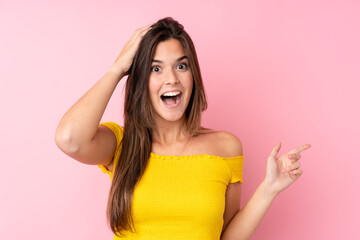 Teenager Brazilian girl over isolated pink background surprised and pointing finger to the side