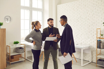 Young serious office workers of different nationalities discuss the project together in a bright office. One woman and two men are looking for ways to solve business problems. Concept of teamwork.