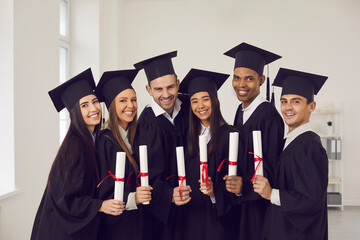 Portrait of a group of happy multiracial university graduates in academic gowns and with diplomas in their hands. Concept of successful completion of an important educational stage in life.