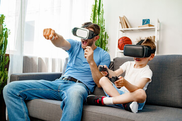 Dad and son sitting on sofa and playing games with VR glasses - Powered by Adobe