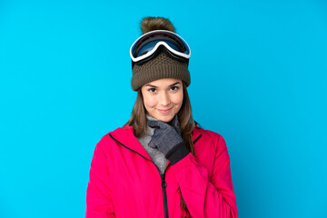 Teenager skier girl with snowboarding glasses over isolated blue background laughing
