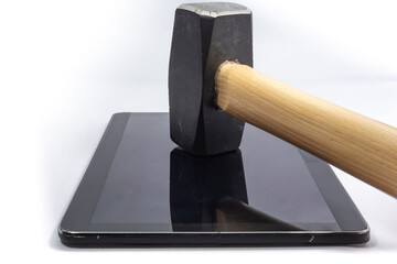 A tablet lays face up with a sledgehammer resting horizontally at an angle, handle towards camera, on the screen. Photo taken from the side.