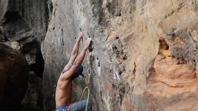 Sportive Man Training On Mountain Wall. Side view of athletic muscular man hanging on high cliff and climbing up.
