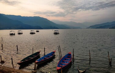 Obraz premium Boats on the lake in pokahara,Nepal. fishing boat in a calm lake water, old wooden fishing boat, wooden fishing boat in a still lake water.