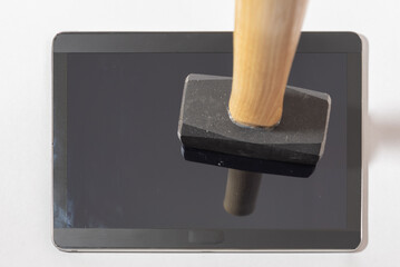 A tablet lays face up with a sledgehammer resting vertically on the screen. Photo is taken from above.