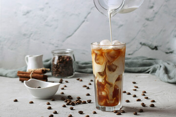 Cold coffee in a tall glass with cream being poured into it showing the texture of the drink. Light gray background, Horizontal format