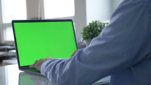 View from the back of man in black shirt sitting at the table and typing on laptop with green chroma key screen. Stock footage. Laptop new technology concept, chroma key green screen