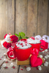 Valentine hot chocolate or coffee, Two red cups with hot chocolate or latte drink, with whipped cream ans sugar heart sprinkles, with roses bouquet ad gift box