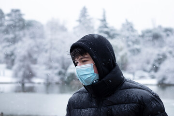 Fototapeta na wymiar boy outside snowing with surgical mask and black coat