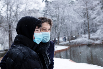 Fototapeta na wymiar father and son in a snowy park with a surgical mask with black coats