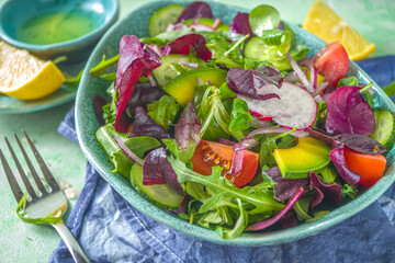 Fresh colorful spring salad - avocado, fresh vegetables, salad leaves and feta cheese, light green concrete background copy space
