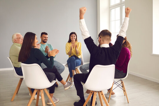 Person Who Managed To Cope With Problem And To Overcome Addiction. Diverse People Sitting In Circle In Group Therapy Meeting And Applauding Happy Young Patient, Celebrating His Successful Recovery