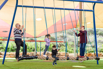 Happy grandparents with cute grandchildren balancing together on a rope on the playground.