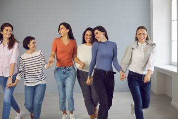 Obraz premium Group of happy smiling carefree young women in their 20s and 30s walking together hand in hand and having fun. Concept of girl power, success, mutual support, female solidarity, confidence in future