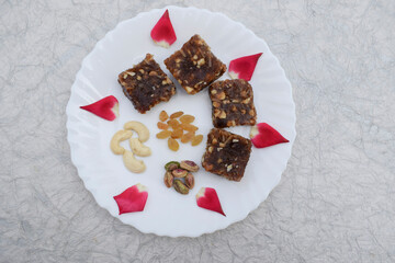 Khajur ka halwa or khajoor paak is a traditional Indian and Pakistani dish. dry fruit halwa barfi dates decorated with red pink rose petals and served during winter season festival like uttarayan