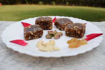 Khajur ka halwa or khajoor paak is a traditional Indian and Pakistani dish. dry fruit halwa barfi dates decorated with red pink rose petals and served during winter season festival like uttarayan