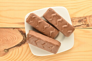 Three chocolate energy bars, on a white saucer, close-up, on a wooden table.